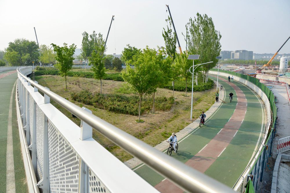 People of all ages and abilities ride bicycles along a green- and orange coloured dedicated and elevated cycle path in Beijing.