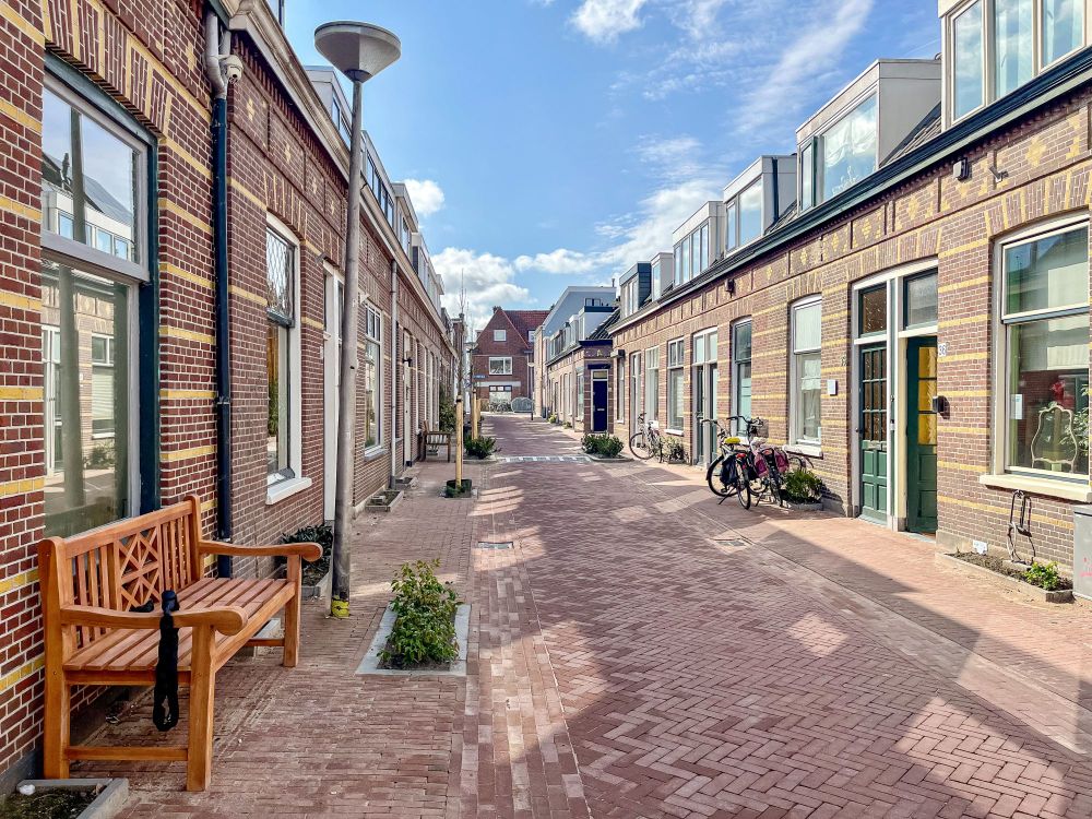 People walk along a “woonerf” or “living street” lined with trees, plants, lampposts, benches, and two-storey brick buildings in Delft, The Netherlands.