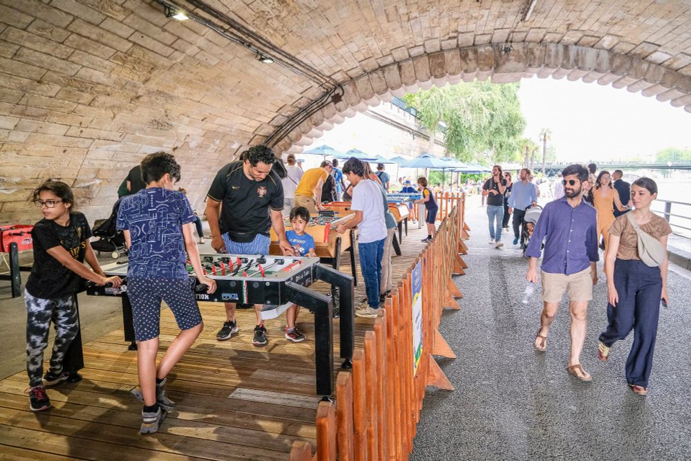 People in casual summer attire walk, cycle, lounge, drink and dine on the “Paris Plages”, an artificial beach installed along the River Seine each summer.