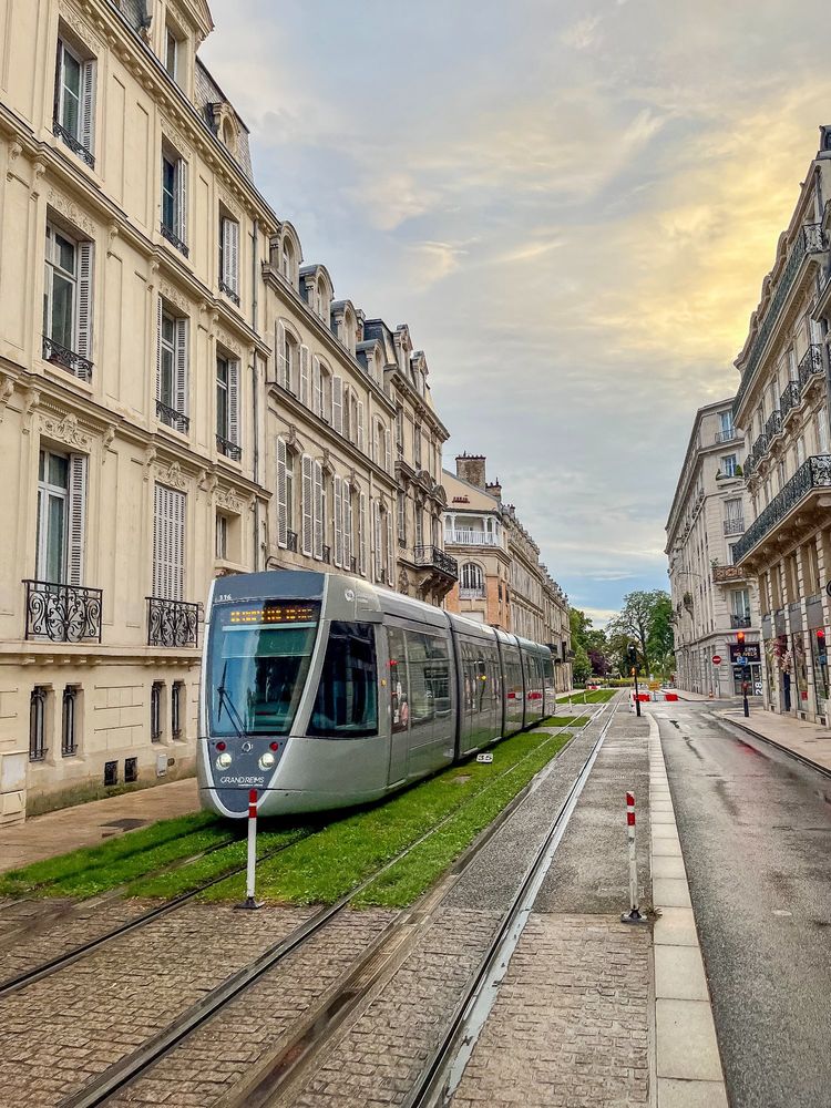 Various photos of colourful trams moving along grassy streets lined with trees and vegetation in Reims, France.