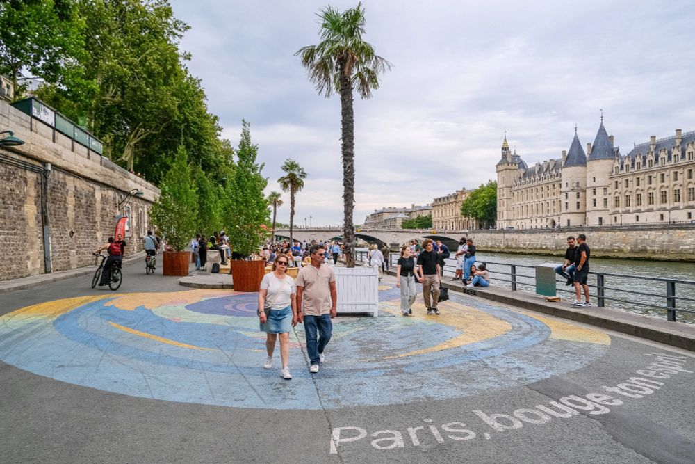 People in casual summer attire walk, cycle, lounge, drink and dine on the “Paris Plages”, an artificial beach installed along the River Seine each summer.