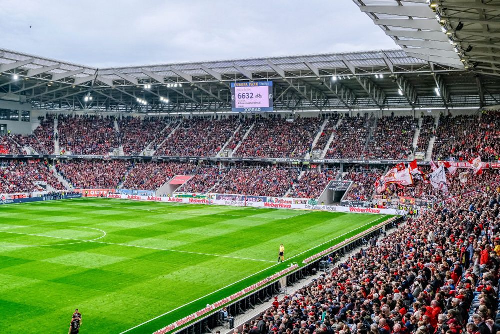 A full stadium of fans wearing red and white clothing during a SC Freiburg football match against Union Berlin.