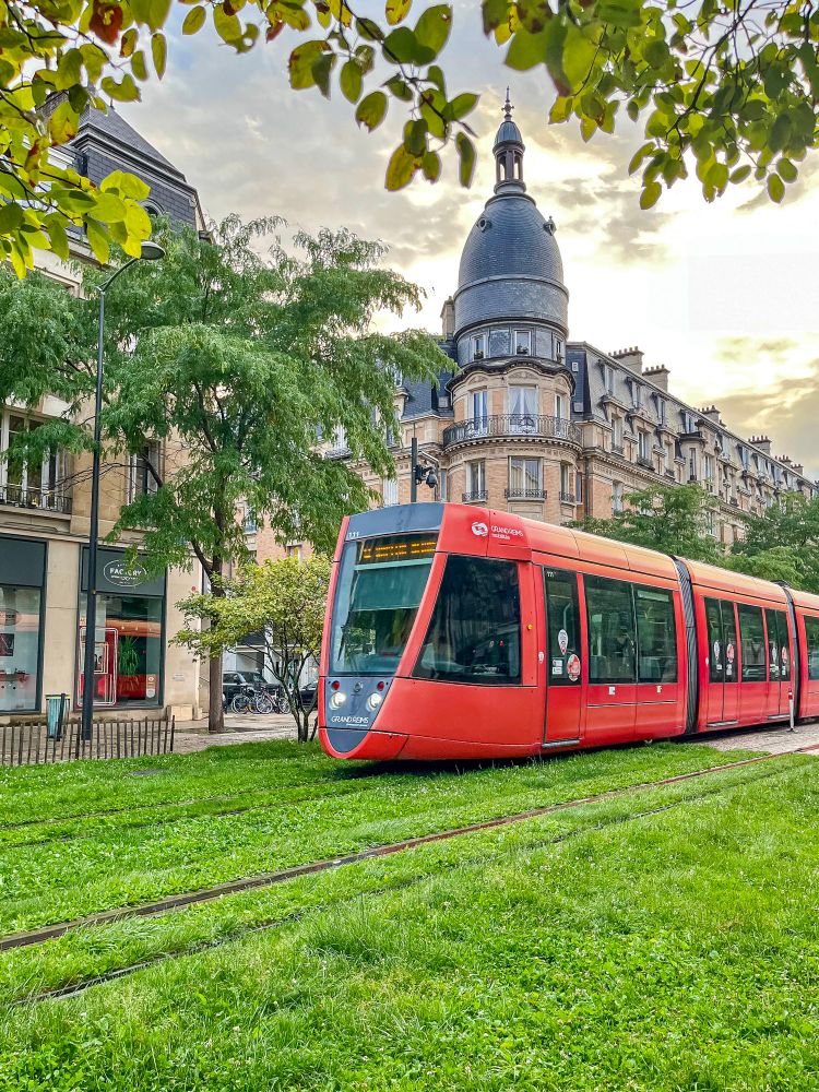 Various photos of colourful trams moving along grassy streets lined with trees and vegetation in Reims, France.