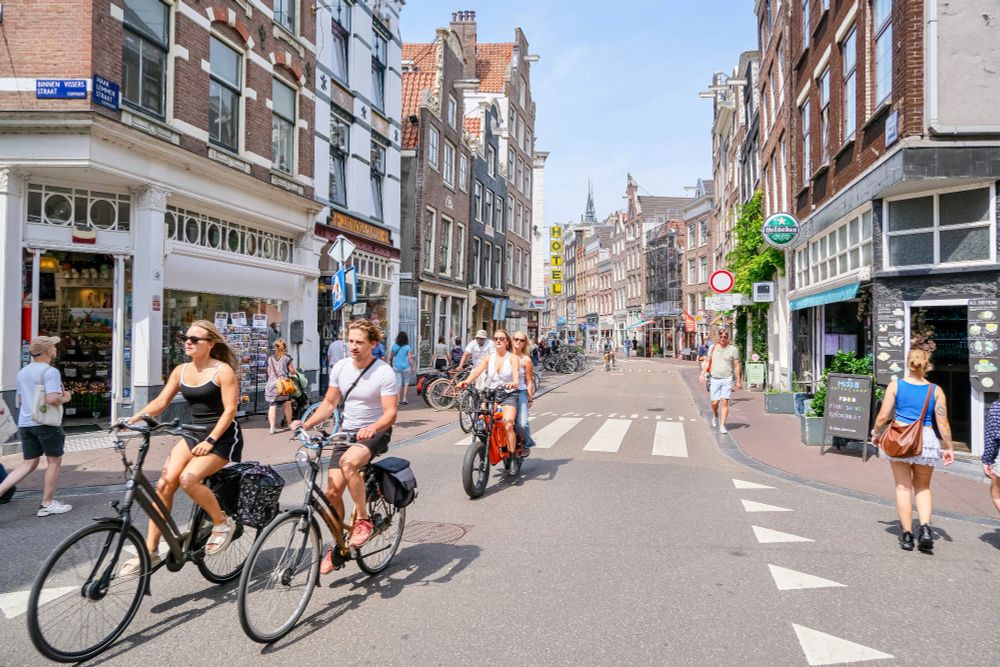 People of all ages and abilities walk, cycle, and drive along the low-traffic streets of Amsterdam, which are lined with buildings, trees, bike infrastructure, and prominent 30 km/hr signage.