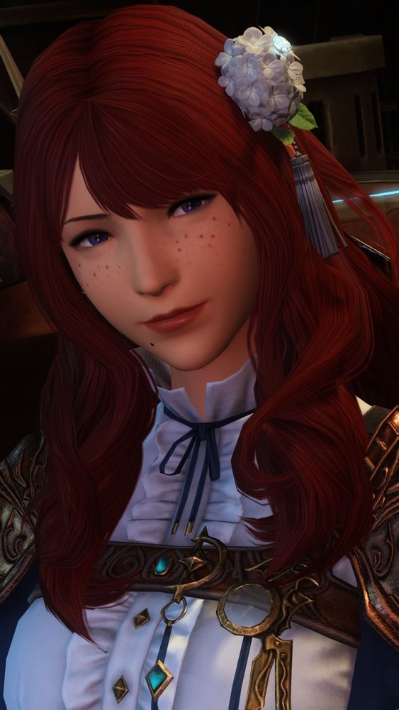 Annabelle, a red-haired Hyur with blue eyes and freckles, smiles at the viewer. She's wearing a white and blue top and a white hydrangea corsage in her hair. 