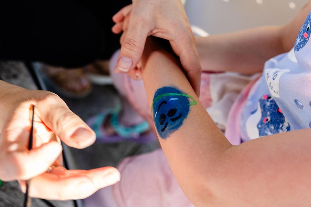 Close-up of four entangled arms, one of them with a smiling happy blue planet painted on it, and a pencil adding finishing touches.