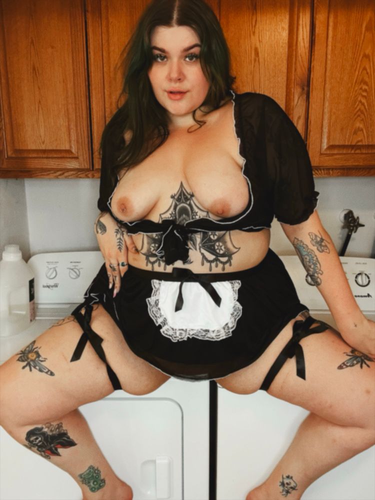 Bratty in a maids costume sitting on a washer and drier with her tits out