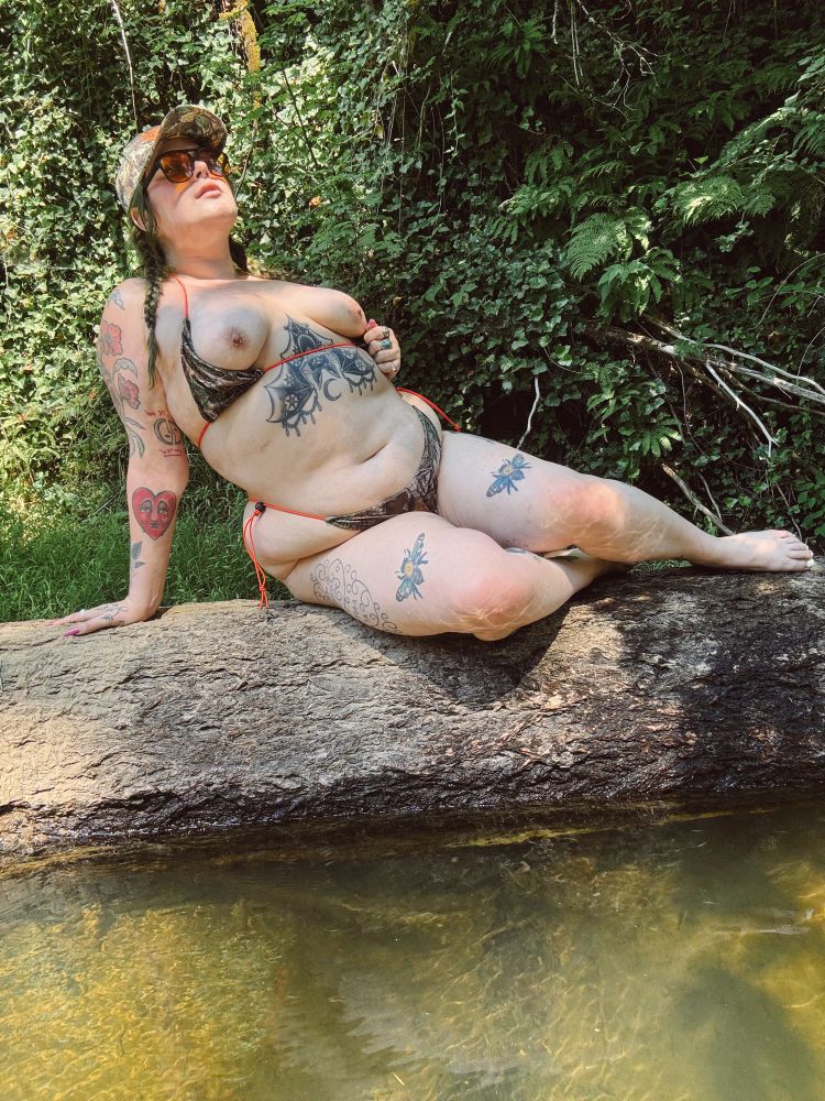 Bratty in a camo bathing suit and hat on a log with her tits out