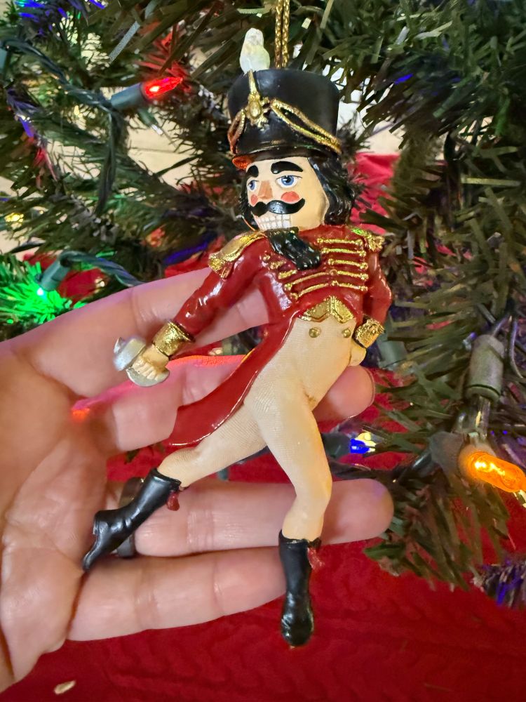 Nutcracker posing with legs half opened, one arm placed along back leg and other arm around waist. 