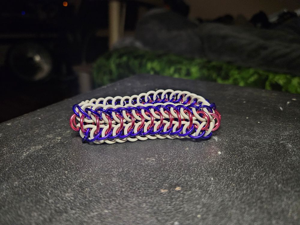 A chainmail bracelet made out of metal and rubber rings that are white purple and pink