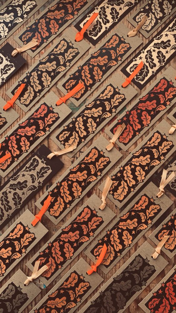 Handmade bookmarks arranged on a wooden board. The bookmarks are hand printed with autumn leaves in various colours. Each bookmark has a ribbon attached. 