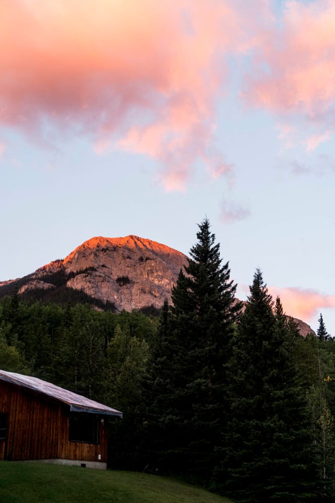 a cabin at sunrise with a mountain in the background and trees in the middle ground