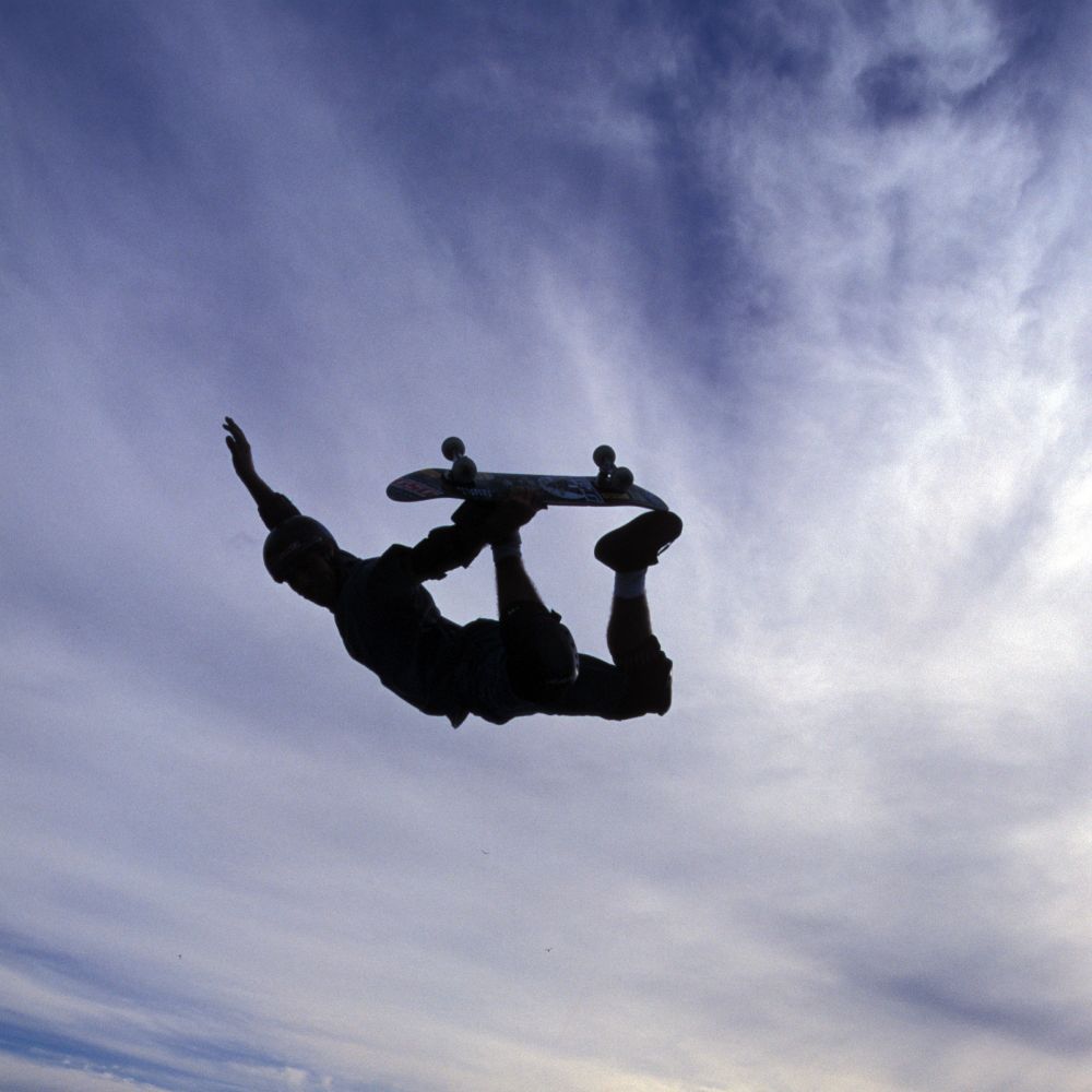 Silhouette of a skateboarder in a mid-air grab with a cloudy blue sky as the background