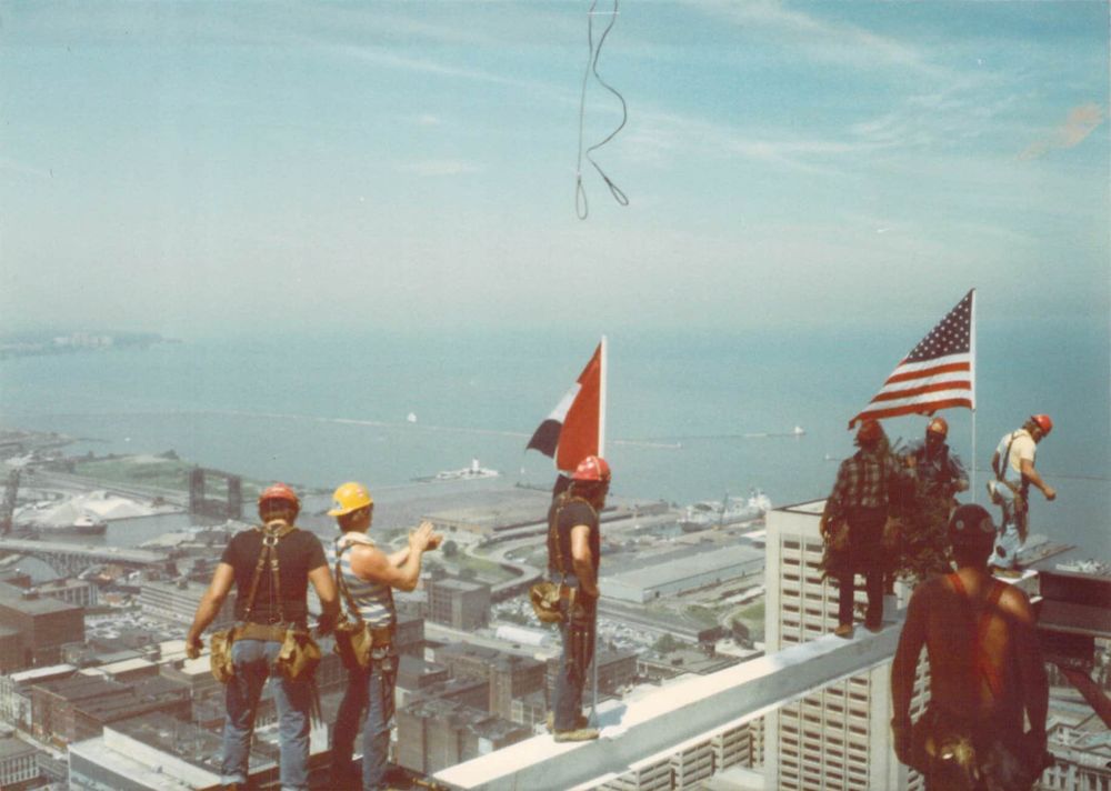 The final piece of steel being put in place for Cleveland’s Sohio Building, probably 1984. Local 17 Ironworkers stand atop a beam with the US and Cleveland flags mounted, with the Lake Erie shoreline in the background.
