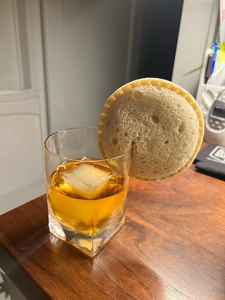 A rocks glass full of whiskey with an Uncrustable affixed to the rim as a garnish.