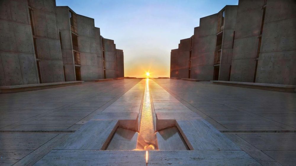 Louis Khan Silence and Light. A setting sun casts a golden glow across a stream of water in the middle of a large concrete plaza.