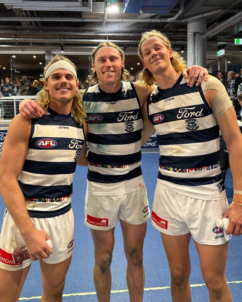 Three blonde-haired football players in ascending height wearing blue and white guernseys. Bailey Smith, Mark Blicavs, Sam De Koning.