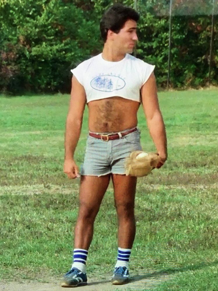 Another man in a cropped white shirt showing off a hairy stomach wearing a denim shorts on a baseball field.