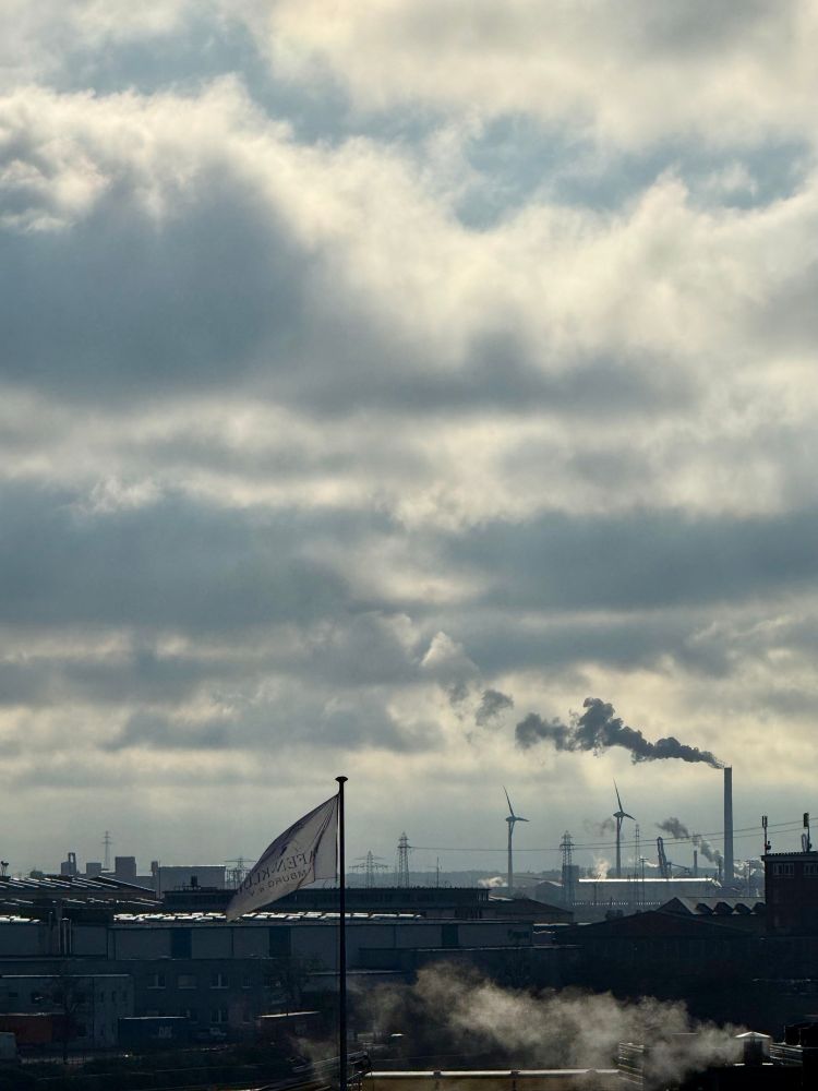 Blick auf den Hamburger Hafen, der Rauch eines Schornsteins geht in die Wolkenüber