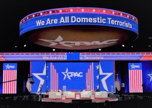 Stage at CPAC displaying "We Are All Domestic Terrorists" banner.