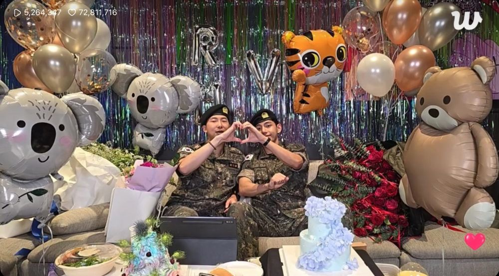 Joonie and Tae making a heart with their hands sitting on the couch during their live.