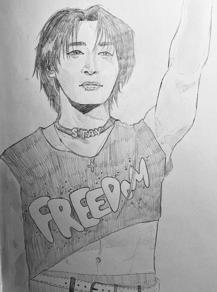 a pencil drawing of I.N from stray kids.
the arm on the viewers right is raised and the left is by his side. his shirt is lifted to reveal his abs. he has on a black shirt with bubble lettering: “FREEDOM” and a choker: “STAY”. 