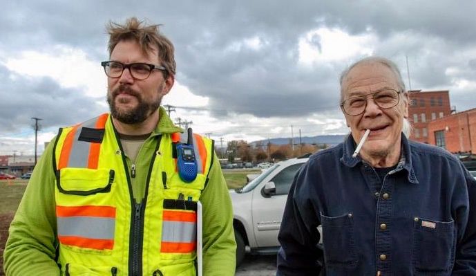 My father visiting my husband as he installed a public art piece called Main Terrain in Chattanooga (my dad’s hometown). Husband is wearing a neon yellow work vest. dad is smiling, and a long cigarette is dangling out of his mouth. 