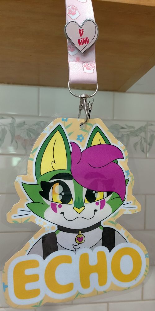 A photo of my new badge by me: it features my cat fursona, Echo, a green, white and pink cat with orange-yellow eyes!

Echo is looking front on at the viewer, smiling softly. Her name sits underneath her in a large font.