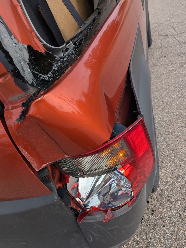 Picture of the rear passenger side corner of a car. The light cover is broken, the bumper is dented, and the side panel is deformed and is 
sticking out at an angle.