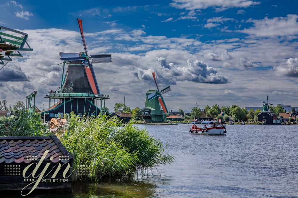 A line of three 17th-18th century dutch windmills in Zaanse Schans. The windmills remain in function today, grinding meal and minerals, sawing lumber, pressing oils... The mills are wooden structures, with thatch roofs. The blades of the mills are a wooden lattice connected the cloth, sail-like material to catch the wind. 