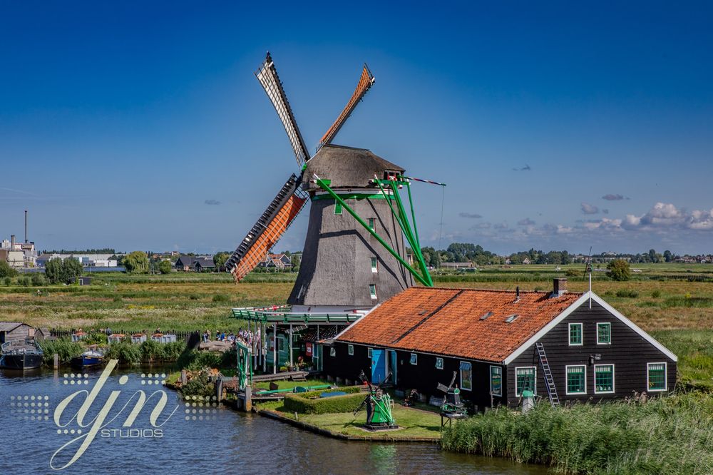 A line of three 17th-18th century dutch windmills in Zaanse Schans. The windmills remain in function today, grinding meal and minerals, sawing lumber, pressing oils... The mills are wooden structures, with thatch roofs. The blades of the mills are a wooden lattice connected the cloth, sail-like material to catch the wind. 