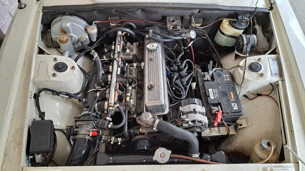 Photo showing the completed engine bay from above following conversion to megasquirt electronic fuel injection. 

In the bottom LH corner, we see the fuse box on the inner wing, and a single throttle body adjacent to that. Left of centre shows the plenum and inlets, with injectors and fuel rail above. Right of centre shows the coilpack, immediately behind the alternator.