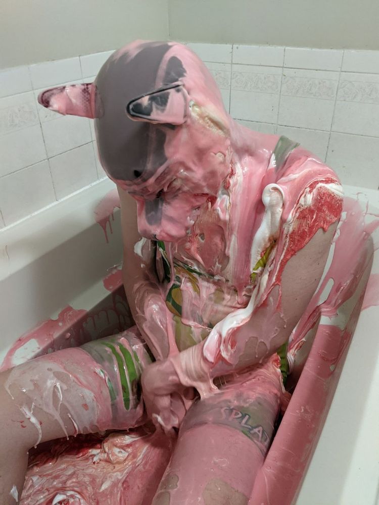 Scani in a pup hood with his arms tucked, covered in pink and white slime in the tub.