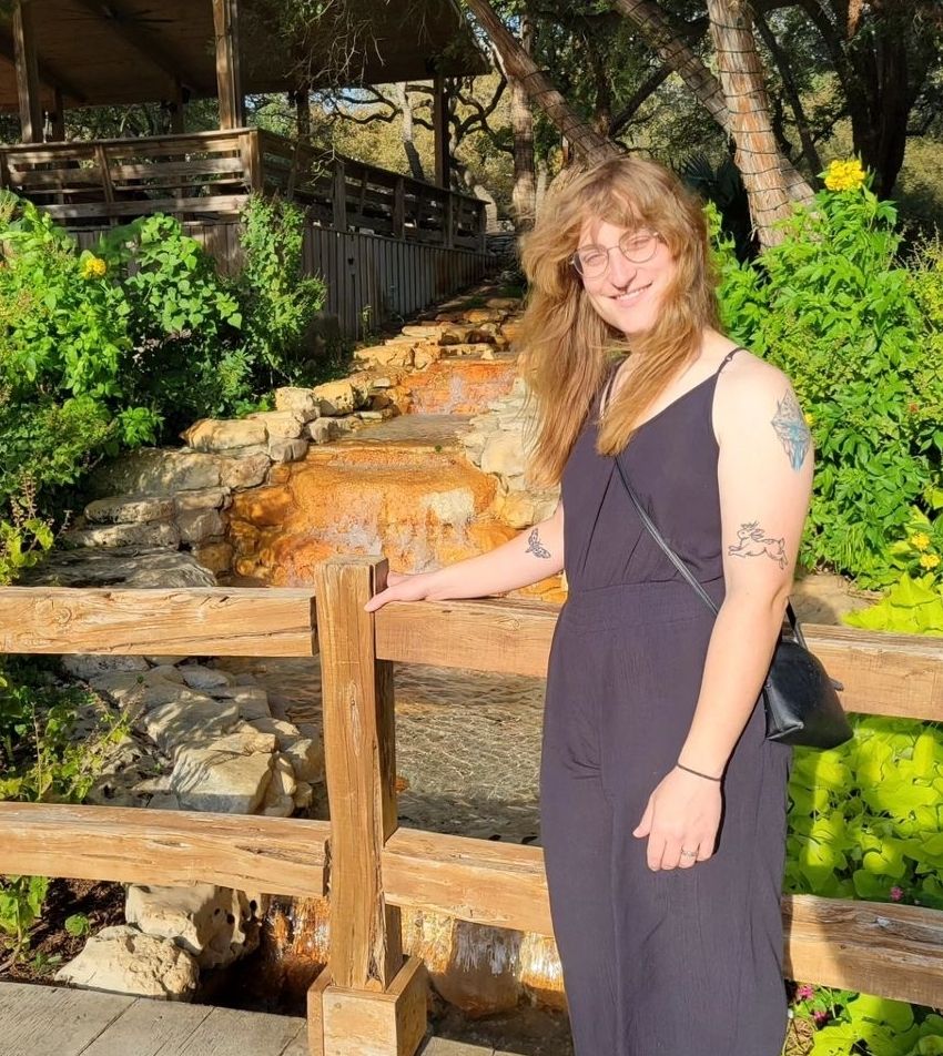 A photo of me in a black romper posing outside by a babbling brook