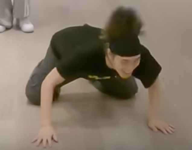 Closeup of Hendery on all fours on the floor, whipping his head up and down. It does not look like a human form.