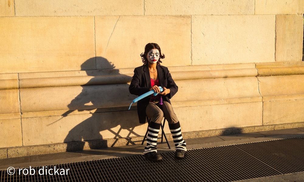 Street mime casting shadow on wall while making a balloon animal