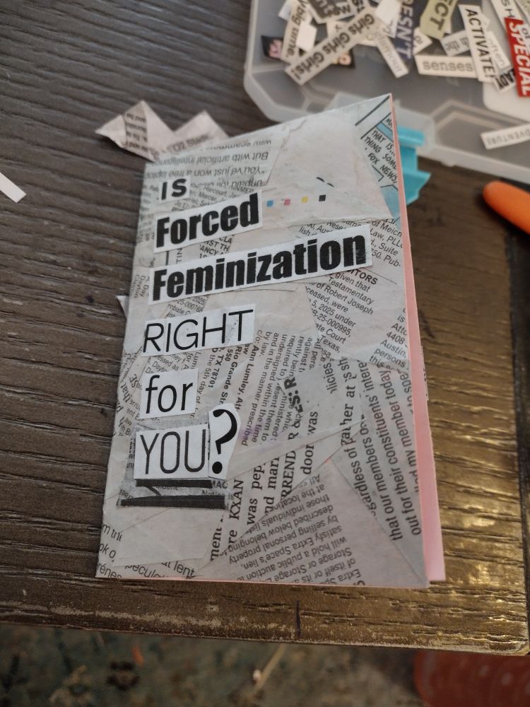 A mini zine on a brown coffee table. The zine is covered in scraps of newspaper, but a bit of the pink copy paper it was glued onto is visible. The zine is titled "IS Forced Feminization RIGHT for YOU?"