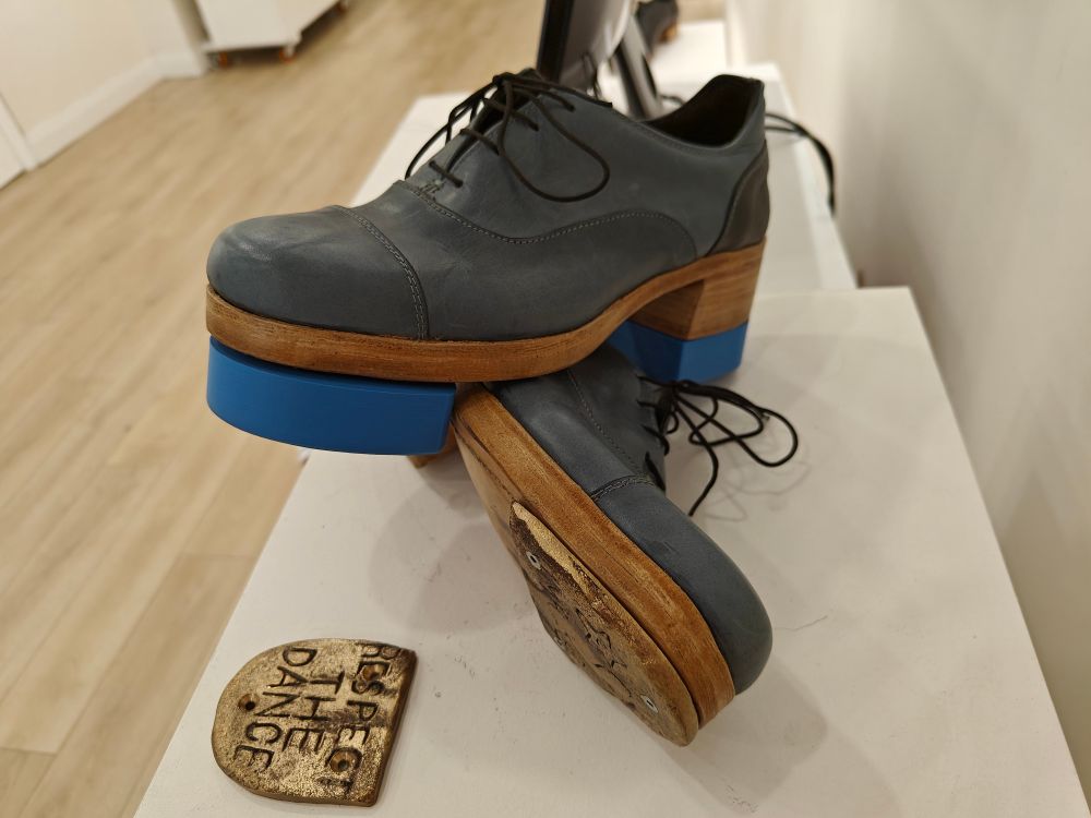 Black leather Oxford style shoes with bronze tap on one shoe and blue plastic taps on thee other