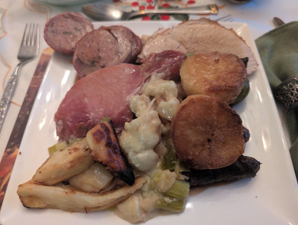 Plate of Christmas dinner including roast potatoes, bacon ribs, parsnips, turkey breast and turkey leg and stuffing rolled in bacon