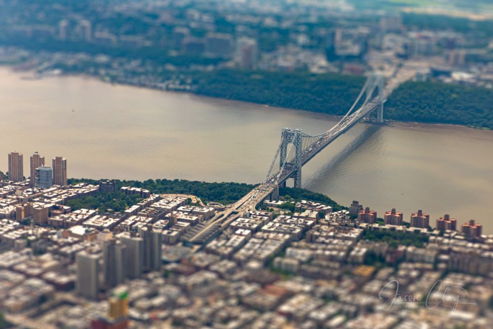 The Georgie Washington Bridge as viewed from high above in an airplane, but the firground and background are out of focus, which gives the impression it's much smaller than it really is. 