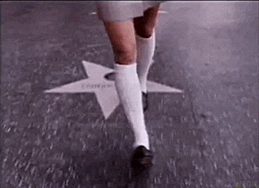 a woman wearing white knee high socks and black shoes is walking on a star on the ground .