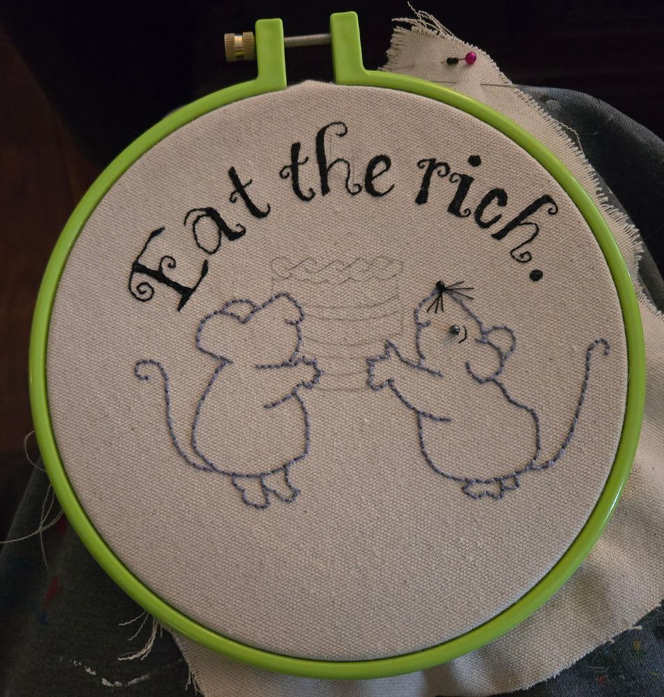 Hand embroidery work in progress of two mice holding up a cake underneath the words "Eat the Rich"