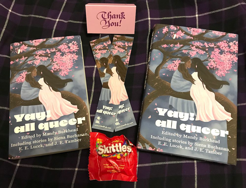 Goodies from Inkd Publishing featuring the Yay! all queer anthology. There are paperback and hardcover versions, two bookmarks, a little thank-you card, and a packet of Skittles.