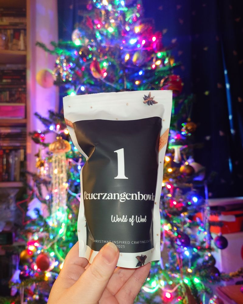 my hand is holding a resealable bag in front of my christmas tree, the bag has a large 1 on and is labelled feuerzangenbowle 