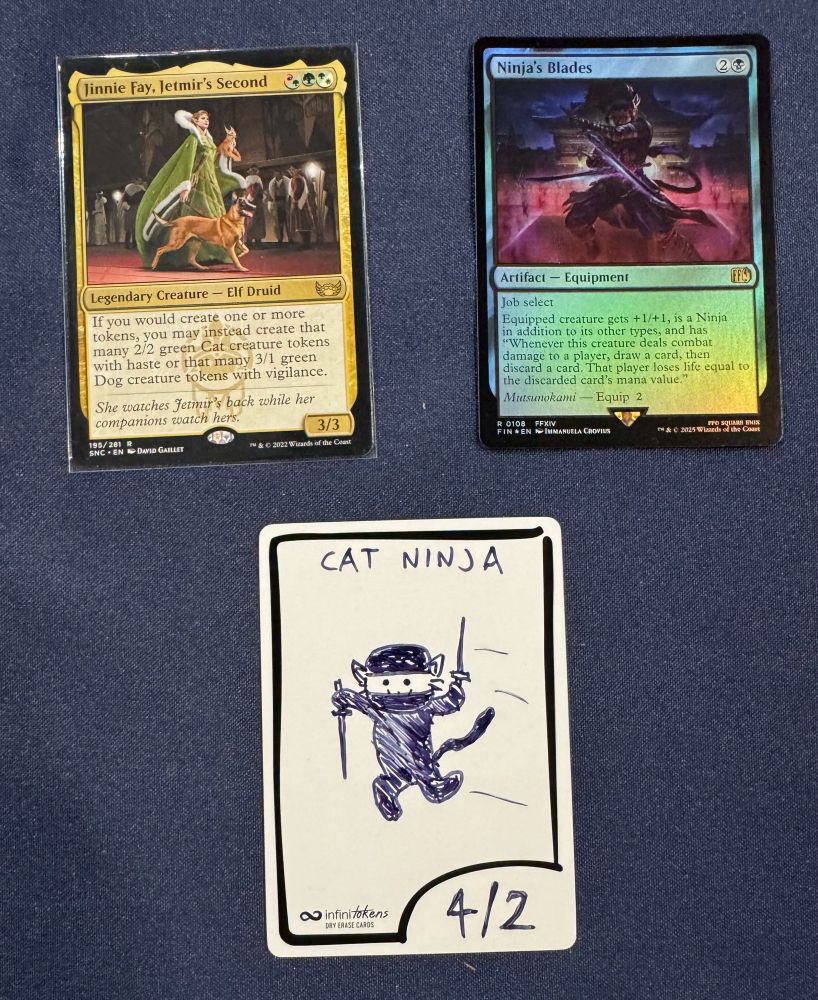 Photo of the MTG cards Jinnie Fay, Jetmir's Second and Ninja's Blades and an Infinitoken. The token is labeled "4/2 Cat Ninja" and depicts a small kitten leaping through the air, clad in black clothes and mask. The cat wields a small dagger in each of two hands, and a small :3 smile can be seen peeking out from underneath the mask.