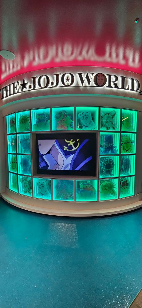 The jojo world wall with Characters both human and stand faces are lighten up by a green light.