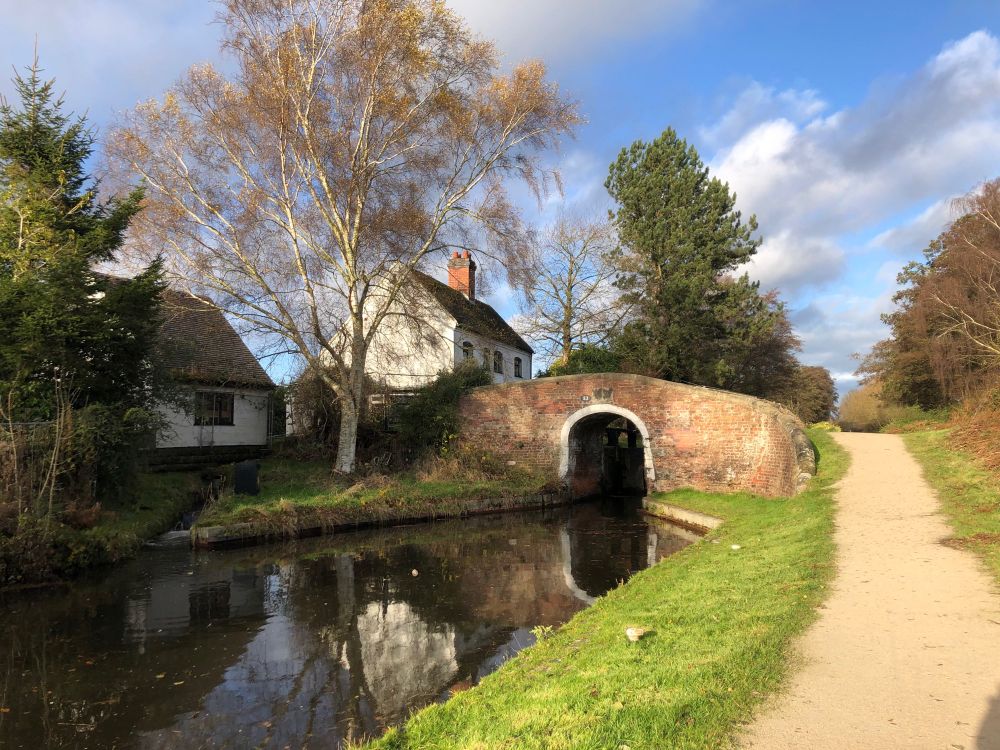 Canal bridge, with canal in foreground and white cottage behind bridge.