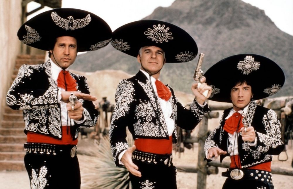 Three men dressed in outlandish cowboy outfits hold pistols. 