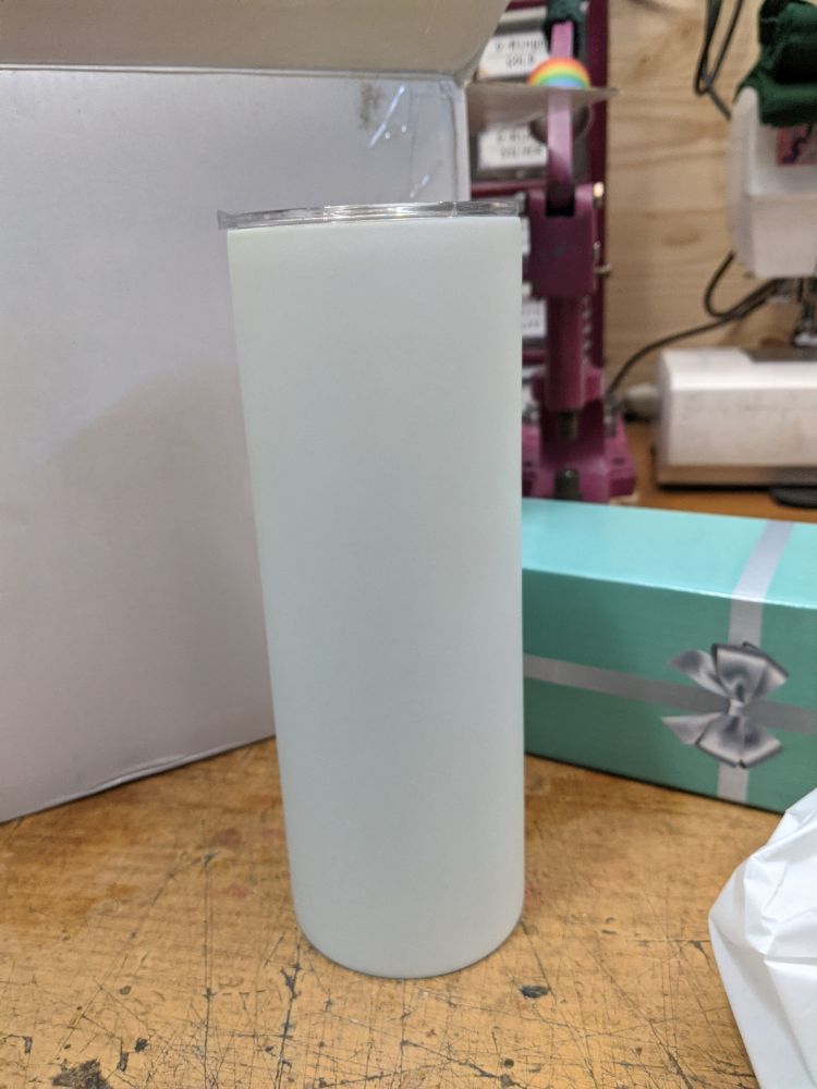 a white tumbler blank on a work table, next to a large box 