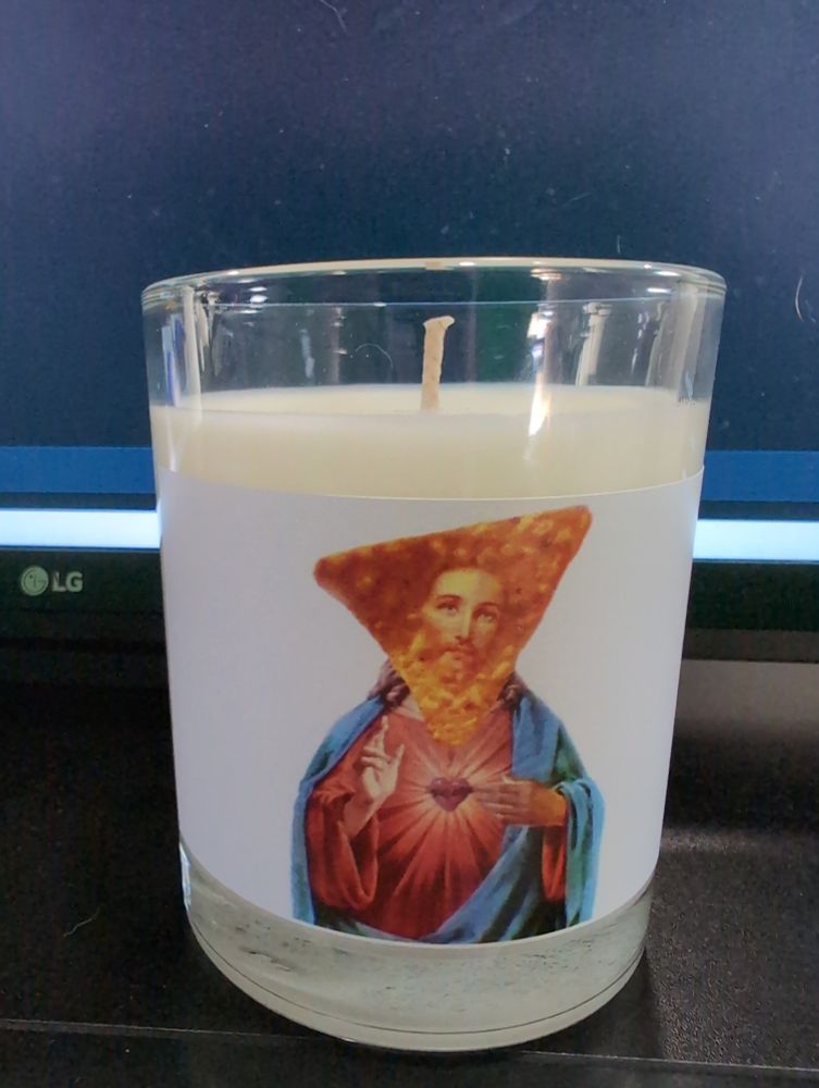 A candle with a Jesus with his face imposed onto a Dorito
